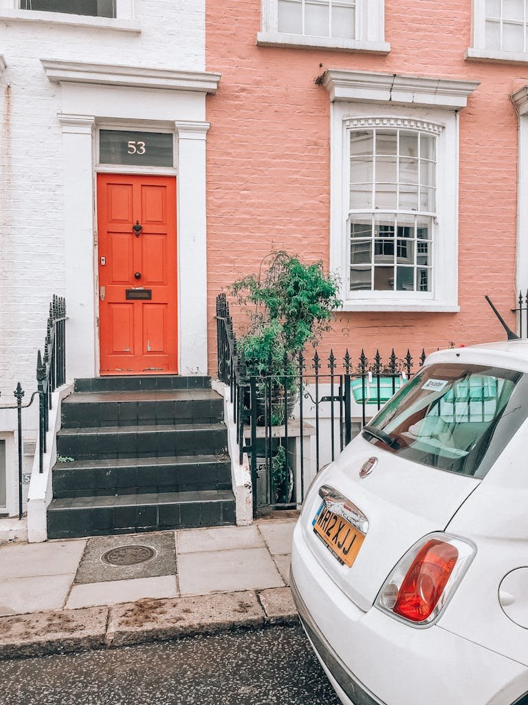 A vibrant red door on a pastel Notting Hill house with a car parked on the street.