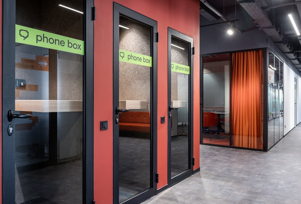 Sleek office corridor featuring modern glass phone booths and vibrant interior design.